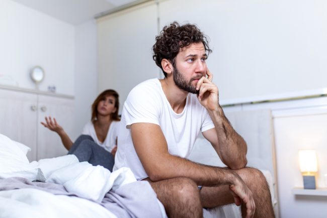 Beautiful girl and a frustrated man sitting in bed and not looking at each other.